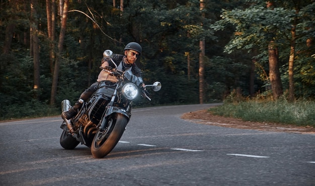 Movimento desfocado um jovem motociclista em um capacete monta rapidamente em alta velocidade em uma estrada florestal em movimento