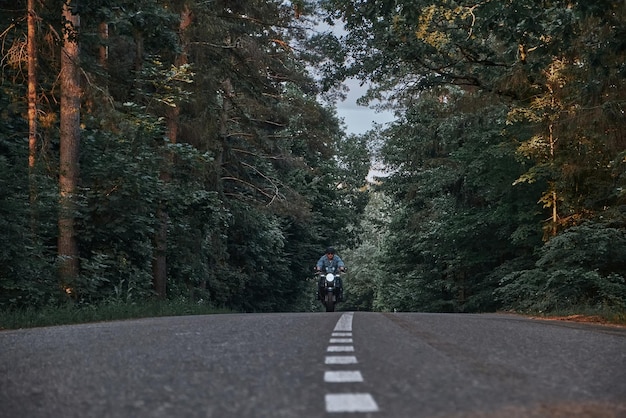Movimento desfocado um jovem motociclista em um capacete monta rapidamente em alta velocidade em uma estrada florestal em movimento