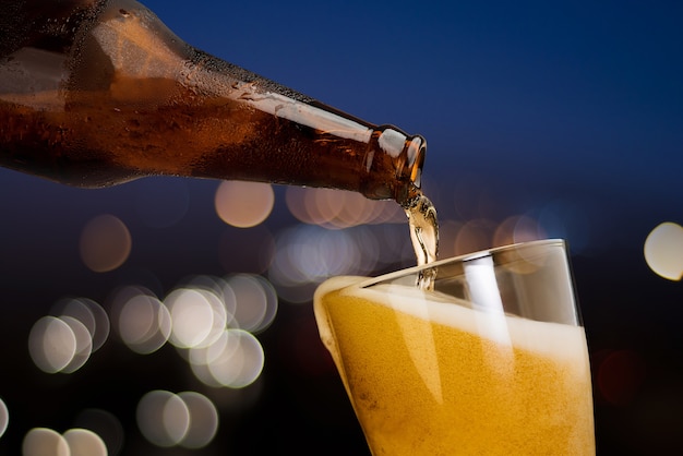 Movimiento de cerveza verter de botella en vidrio sobre fondo de luz bokeh