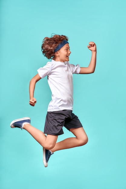 En movimiento disparo vertical de longitud completa de un feliz adolescente lleno de energía saltando aislado sobre azul