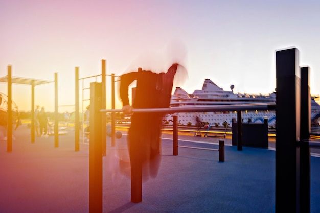 Movimiento hombre borroso en ropa oscura haciendo barra de ejercicios pushup en el campo de deportes de la calle