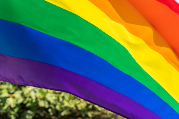 Movimiento LGBT de la bandera del arco iris en el fondo del cielo azul soleado ondear la colorida bandera gay