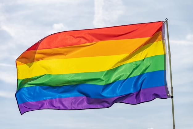 Movimiento LGBT de la bandera del arco iris en el fondo del cielo azul soleado ondear la colorida bandera gay