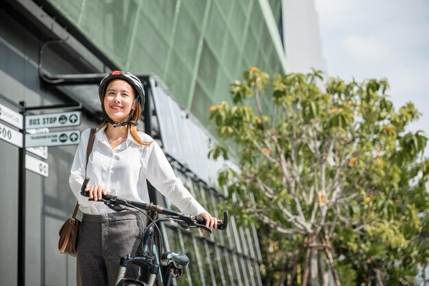 Movimiento matutino y felicidad Una mujer de negocios asiática con casco y traje de pie con su bicicleta Esta imagen retrata el concepto de un viajero de negocios alegre armonizando el trabajo y la actividad al aire libre