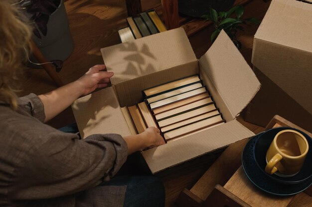 Movimiento de reubicación mujer joven empacando libros en caja de mudanzas