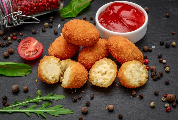 Mozzarella frita, picaduras de queso cheddar, bolas con ketchup sobre tablero de piedra rústica