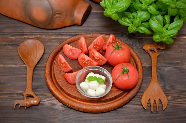 Mozzarella-Kugeln kochen, reife Tomaten und frisches Basilikum auf einem Holzbrett