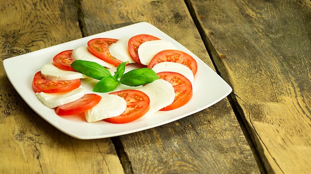 Foto mozzarella mit tomaten auf einem weißen teller auf einem holztisch