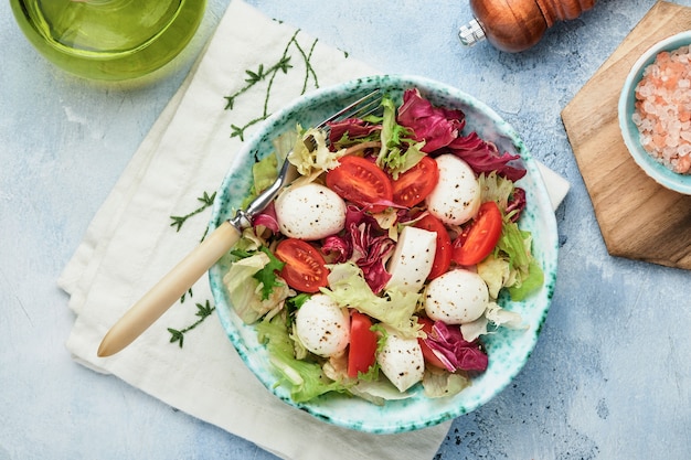 Mozzarella, tomate y mezcla de hojas de ensalada fresca, fondo de mesa de piedra pizarra