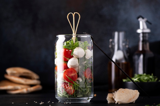 Foto mozzarella con tomates cherry y rúcula en un frasco de vidrio sobre un fondo oscuro