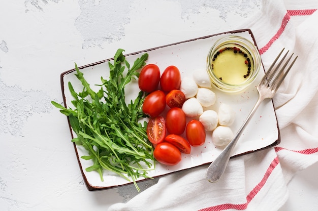 Mozzarella, tomates cherry y rúcula servidos en platos rectangulares de cerámica blanca sobre una superficie de textura gris. Endecha plana