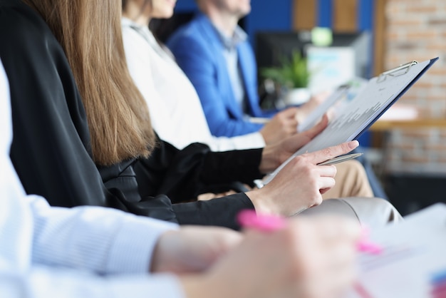 Mucha gente con documentos en sus manos está sentada en primer plano de formación empresarial