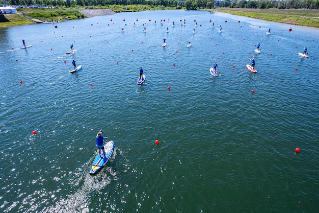 Mucha gente está nadando de pie en el tablero en el agua remando con remos Diversión de verano en el agua SUP en la vista superior de aguas tranquilas