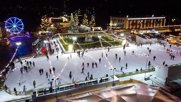 Mucha gente patinando en una hermosa pista de patinaje sobre hielo al aire libre decorada con luces navideñas de año nuevo