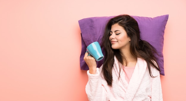 Muchacha del adolescente en la bata sobre backgrounnd rosado y sostener una taza de café