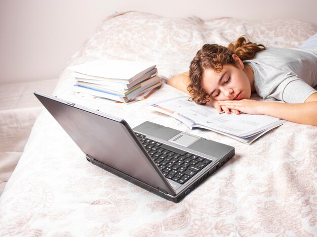 La muchacha adolescente en cuarentena está estudiando en línea en su cama. Niña duerme frente a la laptop