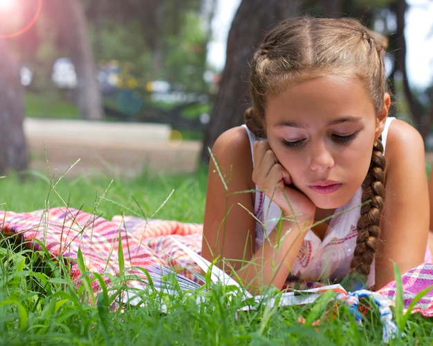 Muchacha adolescente joven que miente en hierba verde y el libro de lectura