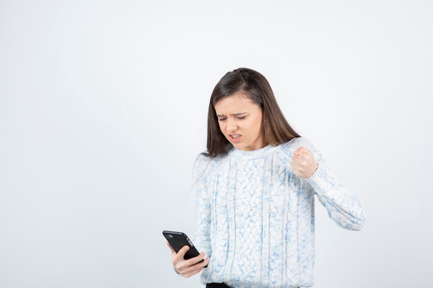 Muchacha adolescente joven que sostiene el teléfono inteligente en el fondo blanco.