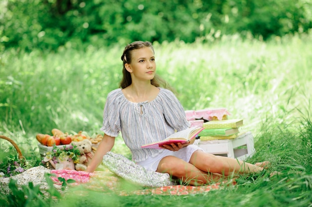 La muchacha adolescente lee un libro en el parque en la naturaleza. La niña hizo un picnic en la naturaleza y se está preparando para la escuela.