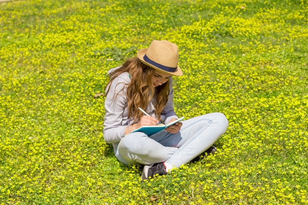 Muchacha adolescente linda que lee un libro en un prado verde.