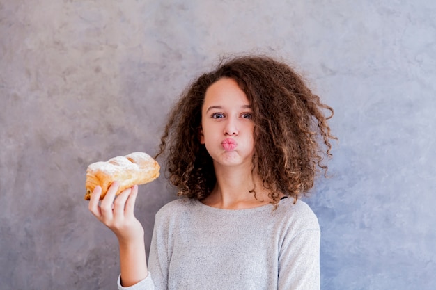 Muchacha adolescente del pelo rizado que come el croissant