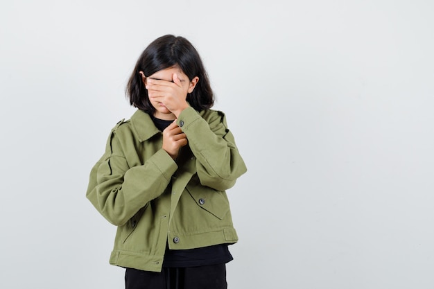 Muchacha adolescente que cubre los ojos con la mano en la camiseta, chaqueta verde y parece cansado. vista frontal.