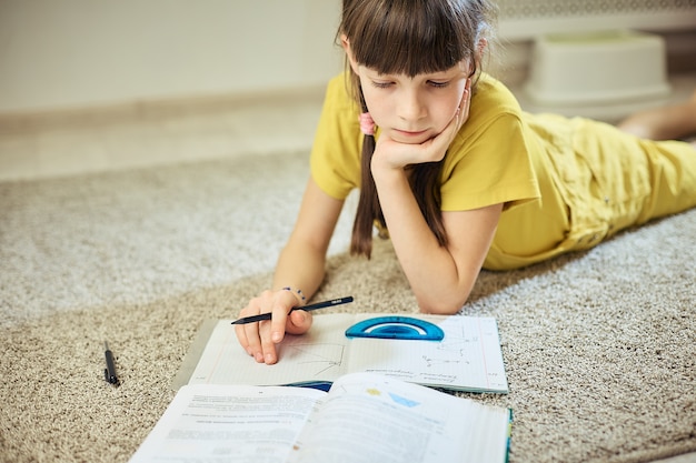 Muchacha adolescente que hace la tarea que se sienta en la alfombra en su sitio