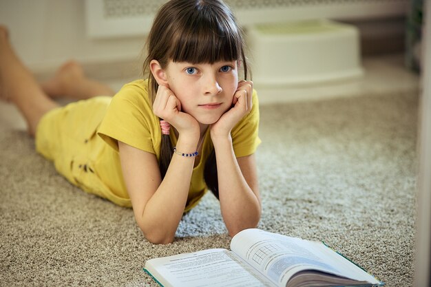 Muchacha adolescente que hace la tarea que se sienta en la alfombra en su sitio