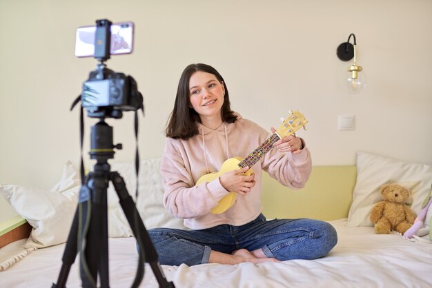 Muchacha adolescente que juega en el ukelele. Blog, canal de música, vlog, chica estudiando online, hablando con seguidores y tocando música