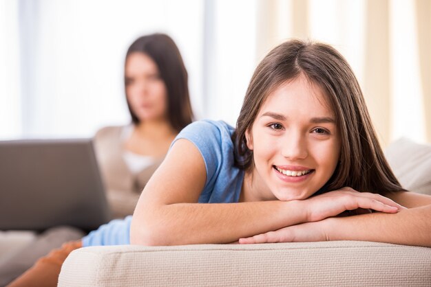 La muchacha adolescente sonriente se está sentando en el sofá y está mirando la cámara.