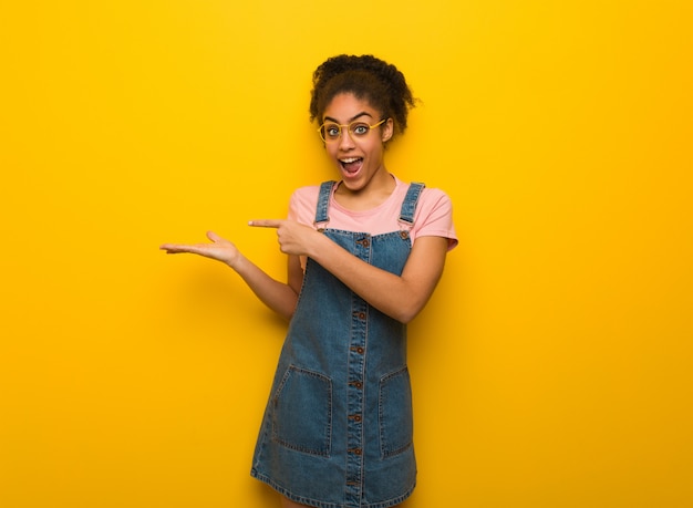 Muchacha afroamericana negra joven con los ojos azules que llevan a cabo algo con la mano