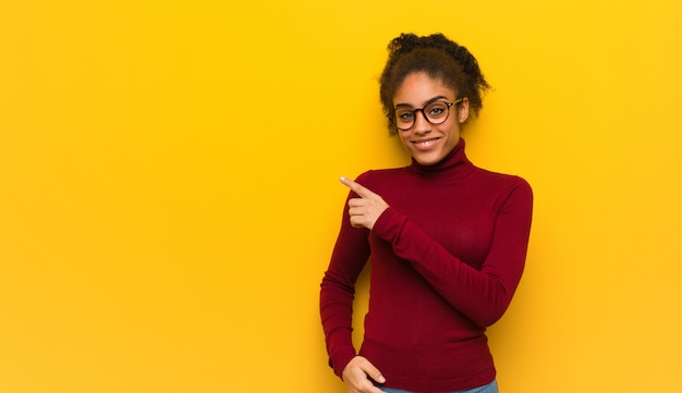 Muchacha afroamericana negra joven con los ojos azules que sonríe y que señala al lado