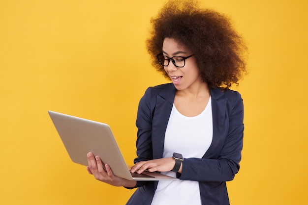 Foto la muchacha afroamericana en traje presenta con la computadora portátil aislada.