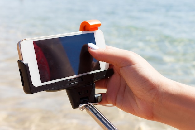 Foto la muchacha ajusta la cámara en el palillo del selfie en el mar