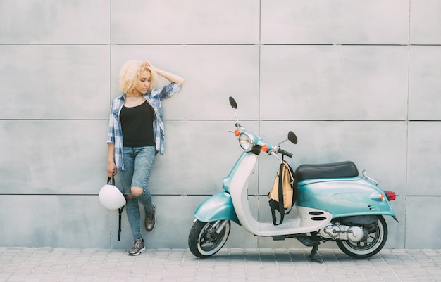 Muchacha alegre joven que conduce la vespa adentro en ciudad. Retrato de una mujer joven y elegante con un ciclomotor