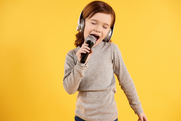 La muchacha alegre pelirroja en auriculares está cantando Karaoke.