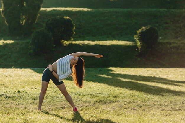 Muchacha de la aptitud que hace estirando ejercicios afuera en la sol una hierba