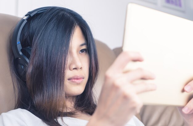 La muchacha asiática con los auriculares está mirando el contenido en la tableta