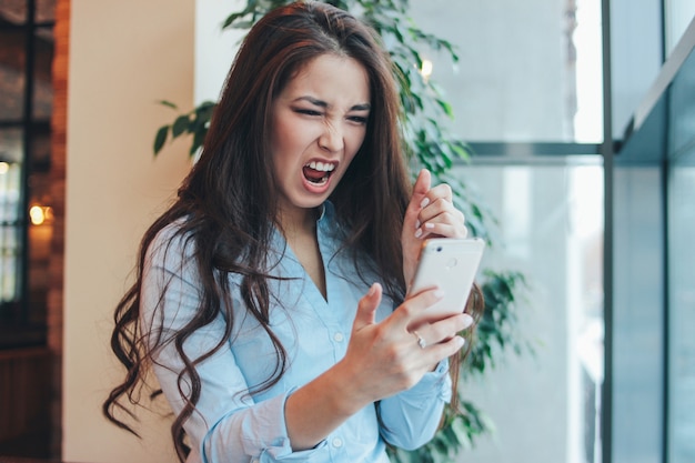 Muchacha asiática enojada morena encantadora hermosa que grita en el teléfono en café