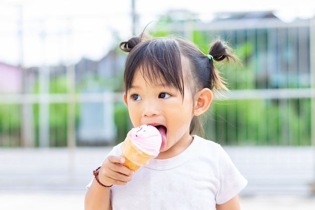 Muchacha asiática feliz del niño que come un helado rosado de vainilla. Temporada de verano,