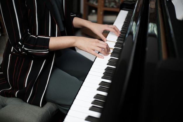 La muchacha asiática hermosa aprende tocar el piano.