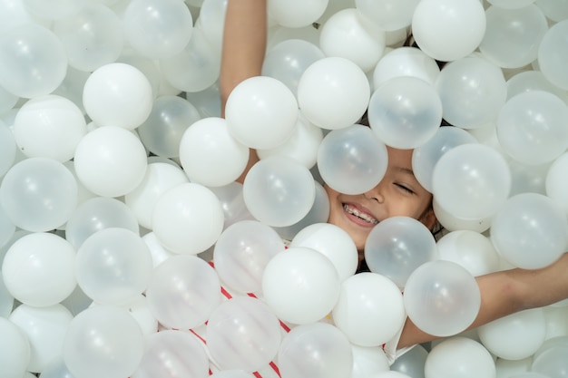 Muchacha asiática linda feliz del niño que se divierte para jugar con las bolas plásticas blancas en el patio