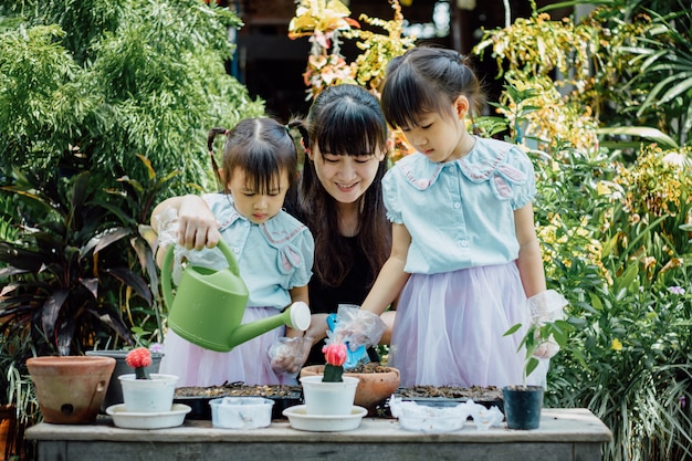 Muchacha asiática linda del niño que ayuda a la madre que planta o cutivate las plantas en el jardín.