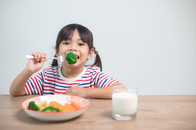 Muchacha asiática linda del niño que come los vehículos y la leche sanos para su comida