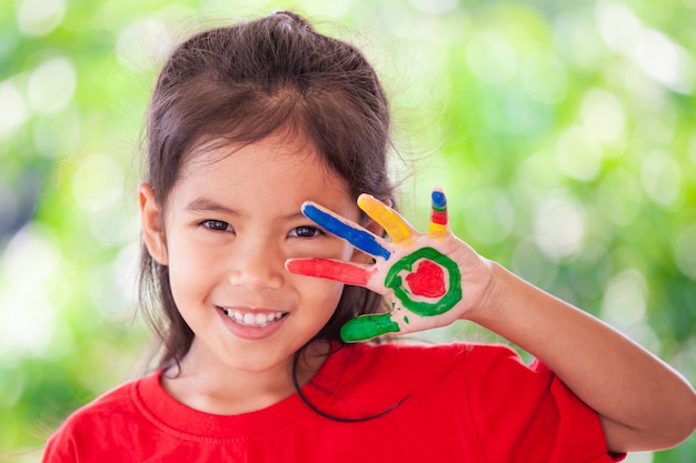 Muchacha asiática linda del pequeño niño con las manos pintadas que sonríe con la diversión y la felicidad