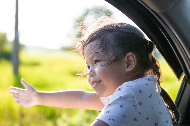 Muchacha asiática linda del pequeño niño que sonríe y que se divierte para viajar en coche.