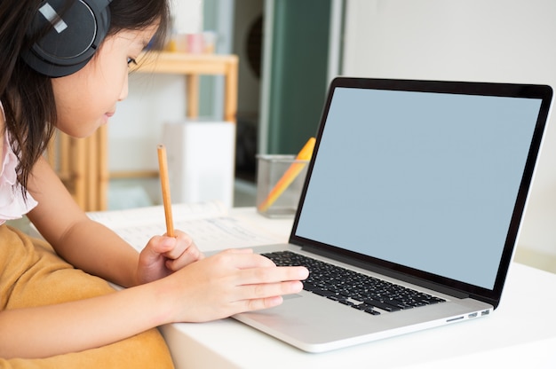 La muchacha asiática linda usa la computadora portátil para estudiar la lección en línea durante la cuarentena casera.