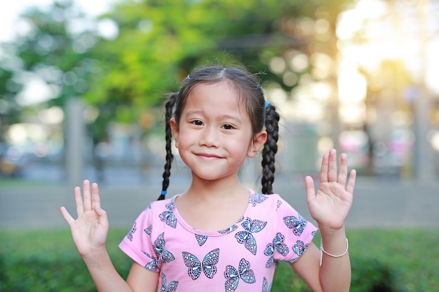 La muchacha asiática del niño o del niño sonríe y muestra sus manos en el jardín al aire libre.