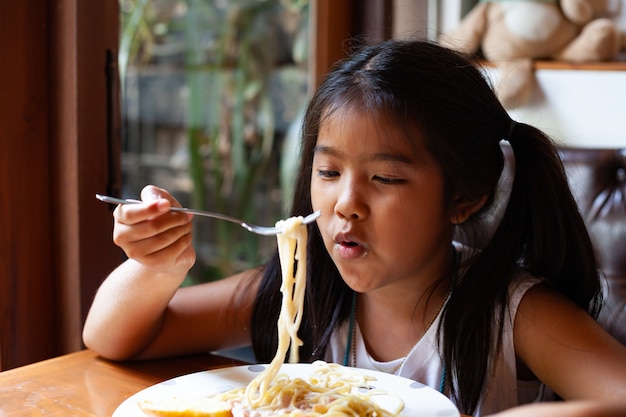 Muchacha asiática del niño que come delicioso Spaghetti Carbonara en el restaurante