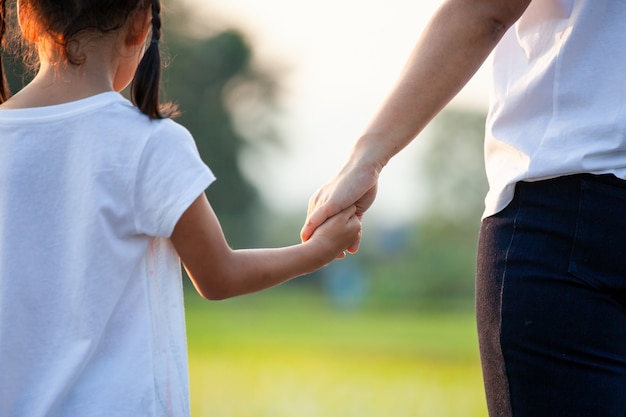 Muchacha asiática del niño que lleva a cabo sus manos de la madre juntas con amor en el campo con luz del sol